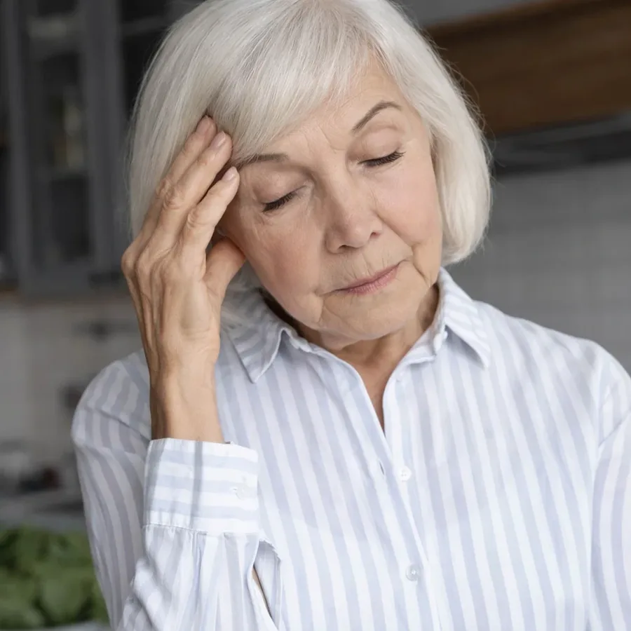 An older woman with her hand on her forehead, eyes closed